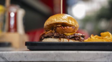 Patates kızartmasıyla servis edilen soğan halkaları ve barbekü soslu gurme Smash Burger.