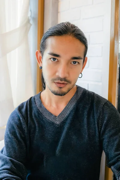 Portrait of a handsome Asian man With long hair, tied my hair to the camera, with the light shining from the back, showing a smooth expression with his reflective mirror on the side
