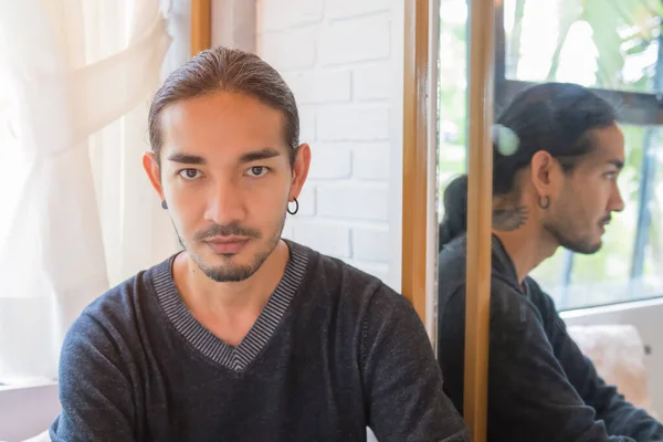 Portrait of a handsome Asian man With long hair, tied my hair to the camera, with the light shining from the back, showing a smooth expression with his reflective mirror on the side