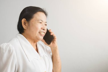 Smiling Asian elderly woman while talking on mobile phone showing happy mood.