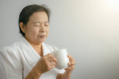 An elderly woman is holding a cup and looking into the cup showing a happy mood with the taste of the drink in the glass.