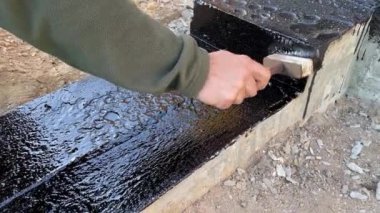 İnşaatçı daha fazla duvar döşemesi için beton temelin tepesine devasa bir astar uygular. 4K video ağır çekim. Temel su geçirmez inşaat çalışmaları