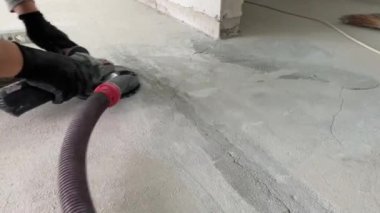 Construction works. Grinding a concrete floor or cement-sand screed to eliminate irregularities before finishing work using a grinder tool and a vacuum cleaner. 4k video footage