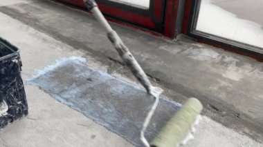 Construction works. 4k video footage with priming the floor surface before further finishing work. The builder is priming the floor with a roller