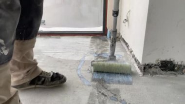 Construction works. 4k video footage with priming the floor surface before further finishing work. The builder is priming the floor with a roller