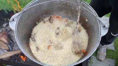 The process of cooking traditional Uzbek pilaf. Close-up footage of a man cooking pilaf in a cauldron on a fire. Slow motion video 4k. A man pours water into a bowl