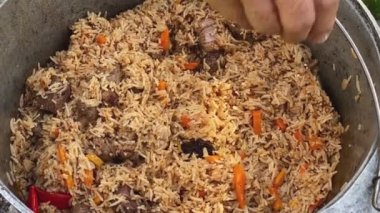 The process of cooking traditional Uzbek pilaf. Close-up footage of a man cooking pilaf in a cauldron on a fire. Slow motion video 4k. Man salting pilaf