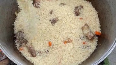 The process of cooking traditional Uzbek pilaf. Close-up footage of a man cooking pilaf in a cauldron on a fire. Slow motion video 4k.