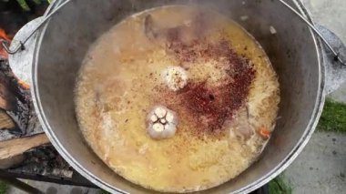 The process of cooking traditional Uzbek pilaf. Close-up footage of a man cooking pilaf in a cauldron on a fire. Slow motion video 4k. A man pours water into a bowl