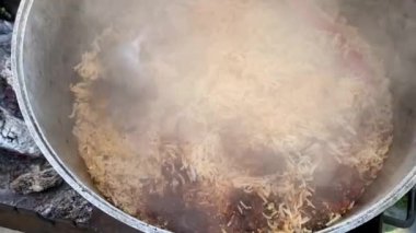 The process of cooking traditional Uzbek pilaf. Close-up footage of a man cooking pilaf in a cauldron on a fire. Slow motion video 4k. A man pours water into a bowl