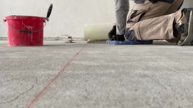 A builder applies tile adhesive to the floor. 4k video footage of construction work on laying tiles. A man using a notched trowel applies a thin layer of adhesive to the subfloor