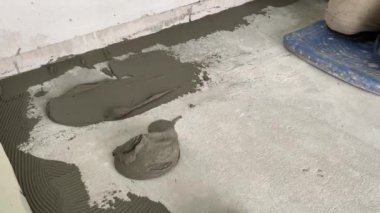 A builder applies tile adhesive to the floor. 4k video footage of construction work on laying tiles. A man using a notched trowel applies a thin layer of adhesive to the subfloor