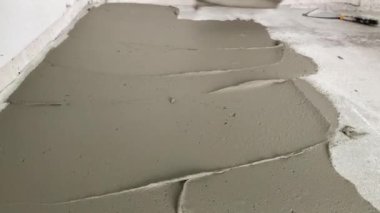 A builder applies tile adhesive to the floor. 4k video footage of construction work on laying tiles. A man using a notched trowel applies a thin layer of adhesive to the subfloor