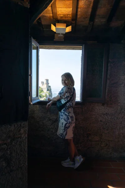 Young beautiful woman visits the sights of the Republic of San Marino, Italy. She stay near the window in Second tower - Cesta and admiring the view from the window on the panorama of San Marino and