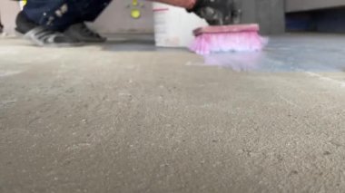 Priming the floor with a brush. A worker applies a primer to the floor surface to increase adhesion. Finishing work in the room. Construction work indoors