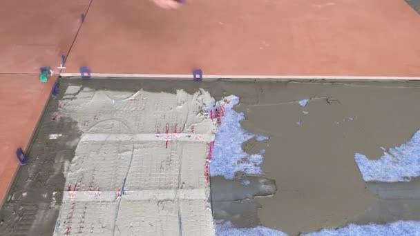4K视频镜头 将一个大的宽格式橙色瓷砖放在安装的迫击炮上 将瓷砖铺在水泥砂浆上 用于在有地热系统的表面粘贴瓷砖 — 图库视频影像