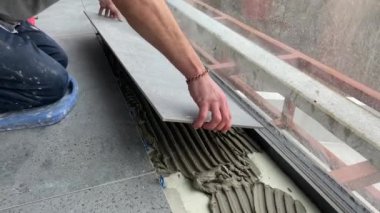 4k video footage of laying a large wide-format tile on a mounting mortar. Tiler laying tiles on cement mortar for gluing tiles on a surface