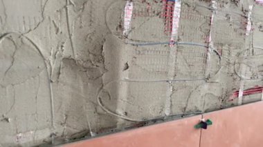 Yükselen bir havan topuna geniş formatlı turuncu fayans döşeme görüntüsü 4K. Döşeme ısıtma sistemi olan bir yüzeye fayans yapıştırmak için çimento harcı döşeyen Tiler.