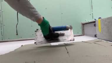 4k video footage of laying a large wide-format orange tile on a mounting mortar. Tiler laying tiles on cement mortar for gluing tiles on a surface with a floor heating system