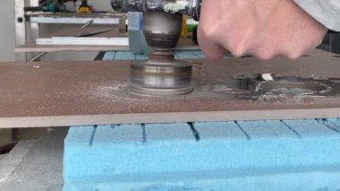 Worker tiller drills round hole in porcelain tile with a diamond core.Drilling labor with tiles, granite or concrete products with electric tile cutter machine with water cutting. Close-up, selective
