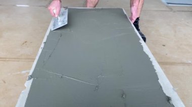 4k video footage of laying a large wide-format tile on a mounting mortar. Tiler laying tiles on cement mortar for gluing tiles on a surface