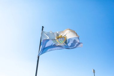 Flag of San Marino in front of blue sky fluttering in the wind