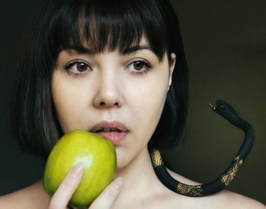 Kısa saçlı ve elinde yeşil bir elma olan bir kız boynunda yapay bir yılan var.