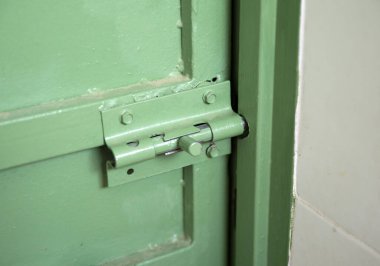 Demir yeşil kapı içeriden sürgülenmiş, sürgü yakın plan sökülmüş, güvenlik için eski.