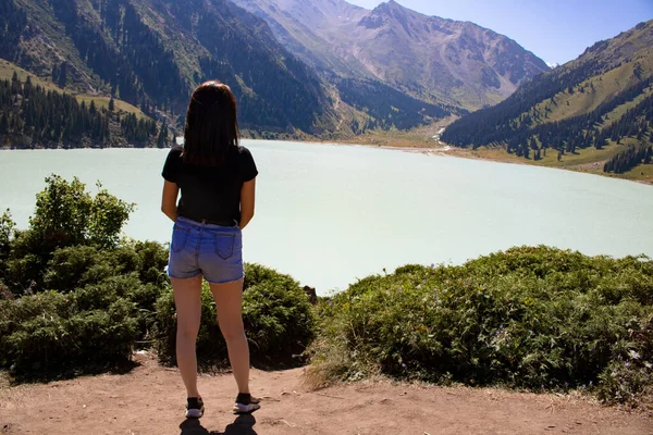 stock image Young happy girl wearing jeans, standing in mountain and looking to lake, Kazakhstan