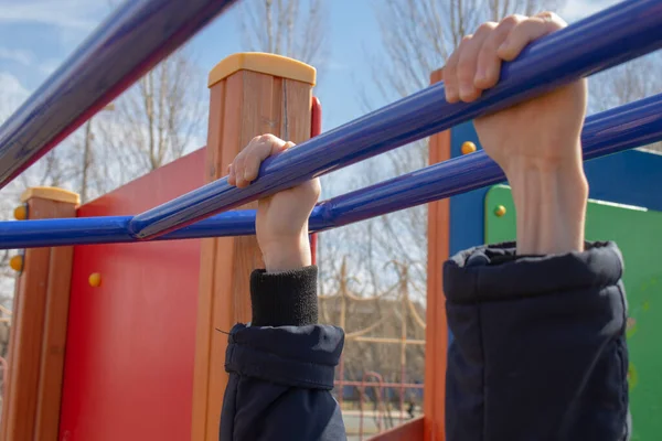 kid hanging on horizontal bar in playground, close-up