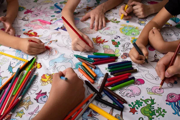 Kids hands holding wax crayons and drawing. Closeup.