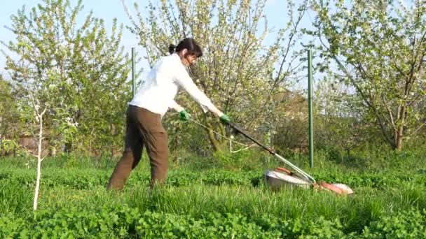 一个女孩在花园里用电动割草机割草 — 图库视频影像
