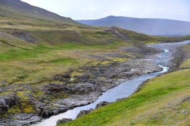 İzlanda 'daki vahşi nehir. İzlanda 'daki yeşil yosunlu tepenin aşağısından akan nehir.