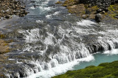 İzlanda 'daki vahşi nehir. İzlanda 'daki yeşil yosunlu tepenin aşağısından akan nehir.