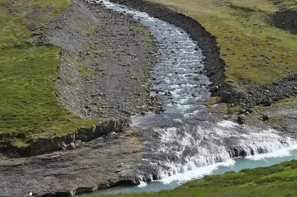 İzlanda 'daki vahşi nehir. İzlanda 'daki yeşil yosunlu tepenin aşağısından akan nehir.