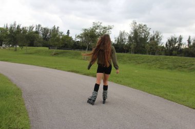 Genç bir kadın parkta paten kayıyor.