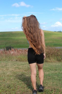 Uzun esmer saçlı ve yeşil tepe arkaplanı olan bir kadın.