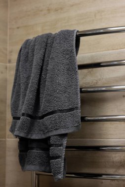 A silver-colored metal bathroom dryer with a gray towel. Electric battery for things and clothes. Horizontal dryer on a beige background made of ceramic tiles with imitation of wood.