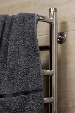A silver-colored metal bathroom dryer with a gray towel. Electric battery for things and clothes. Horizontal dryer on a beige background made of ceramic tiles with imitation of wood.