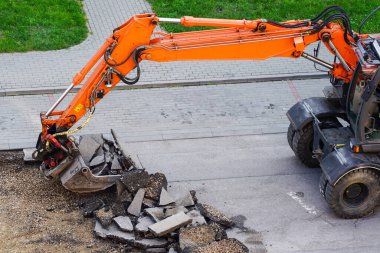Bir kazıcı, eski asfalt tabakasını şehirdeki tamirat sırasında bir kovayla kırıyor.