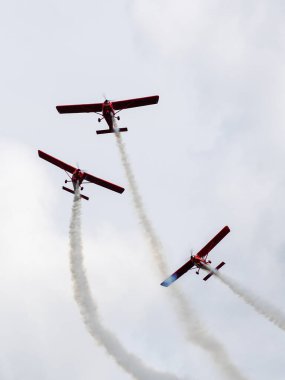 Duman izli üç kırmızı spor uçağı bir hava gösterisi sırasında akrobatik formasyonda uçar.