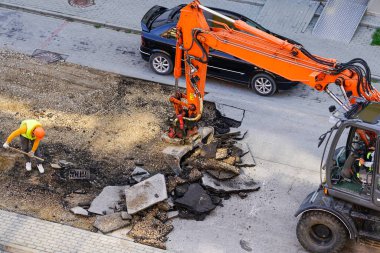 Bir kazıcı, eski asfalt tabakasını şehirdeki tamirat sırasında bir kovayla kırıyor. Kürekle çalışan bir işçi.