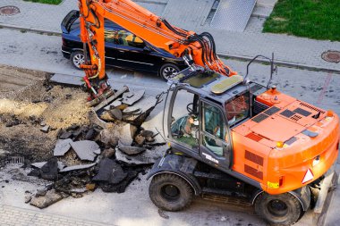 Bir kazıcı, eski asfalt tabakasını şehirdeki tamirat sırasında bir kovayla kırıyor.