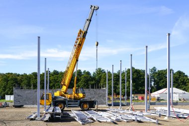 Dikey çelik kolonlar, çelik kirişler ve sarı mobil teleskopik vinç ile modern endüstriyel bir binanın inşaatı