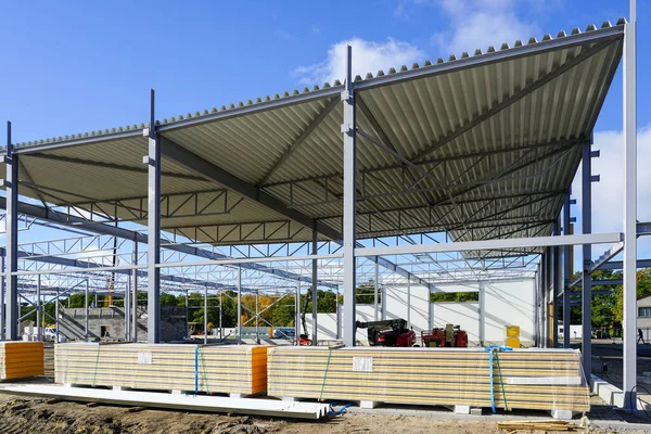 Steel framework with corrugated metal roof panels covering before sandwich panels wall mounting, unfinished warehouse building