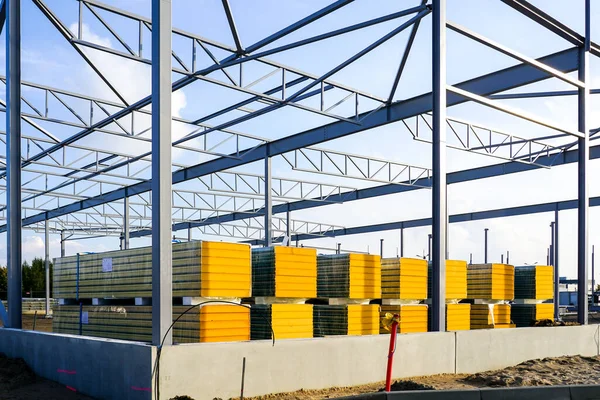 Assembled steel frame and stacks of sandwich panels for the facade of a new modern industrial building