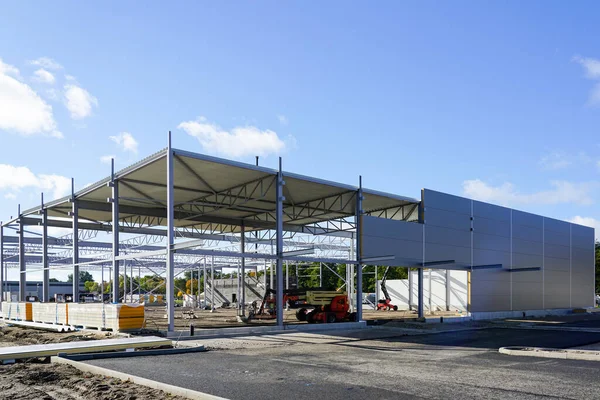 Assembled steel framework with partial assembled sandwich panel wall and corrugated metal roof panels covering of a new warehouse building