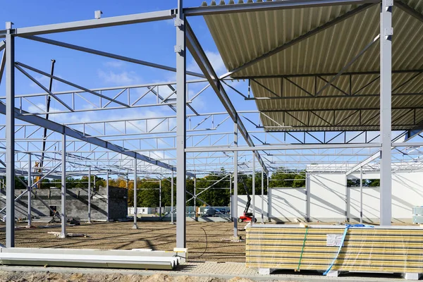Steel framework with partial assembled corrugated metal roof panels covering before sandwich panels wall mounting, unfinished warehouse building