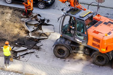 Bir kazıcı, eski asfalt tabakasını şehirdeki tamirat sırasında bir kovayla kırıyor. Kürekle çalışan bir işçi.