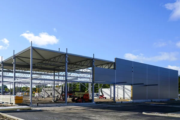 Steel framework with incomplete sandwich panel wall and corrugated metal roof panels covering, unfinished new warehouse building